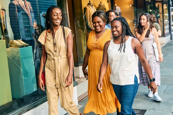 Group of diverse friends walking and smiling on a city sidewalk.