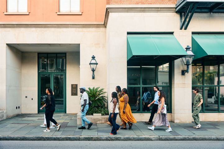 Group of people walking on a city sidewalk past a building with green awnings.
