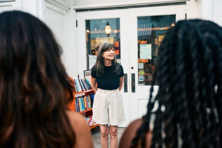 Woman in black shirt and shorts smiling outside a bookstore, with people in the foreground.