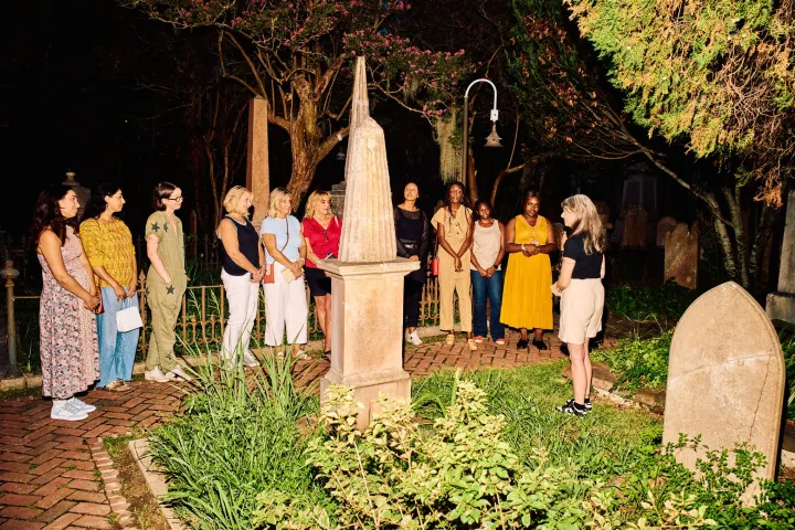 Group of people standing near tombstones in a cemetery at night.
