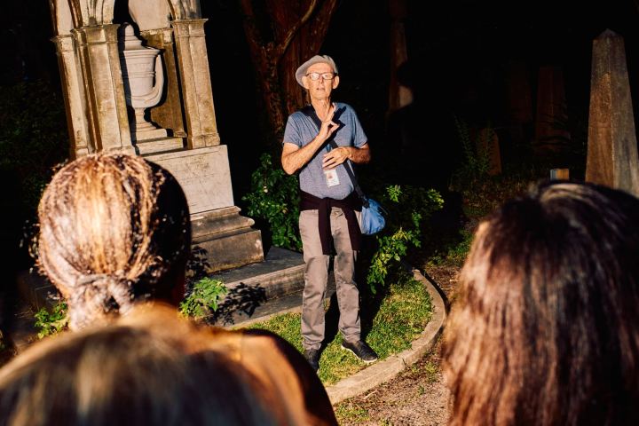 Man giving a tour in a dimly lit cemetery with people listening attentively.