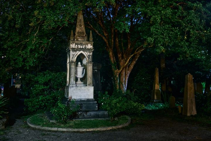 Stone monument with obelisk and urn in a nighttime cemetery setting.