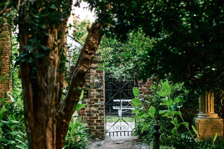 Brick path through lush greenery leading to an ornate wrought iron gate.
