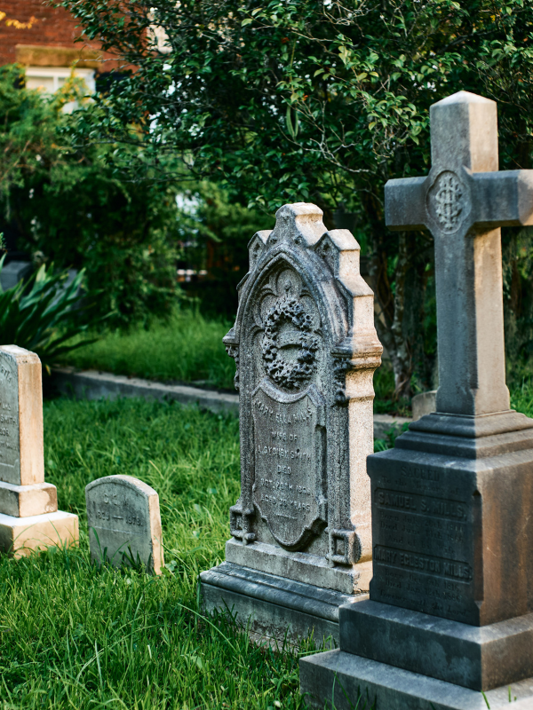 Old gravestones in a grassy cemetery with trees in the background.
